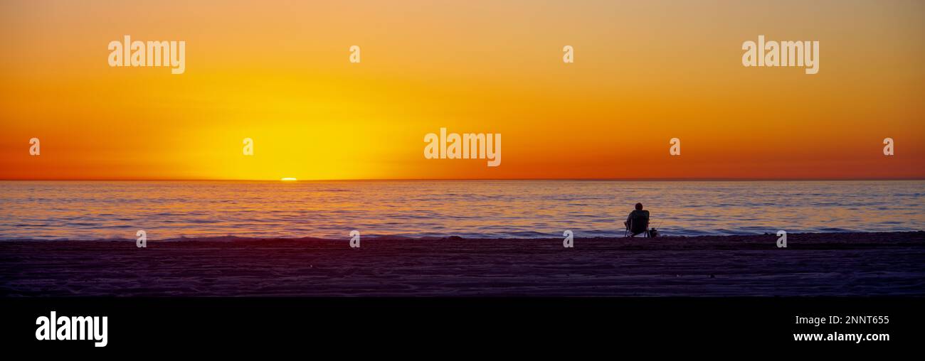 Homme assis sur Manhattan Beach au coucher du soleil, Los Angeles County, Californie, États-Unis Banque D'Images