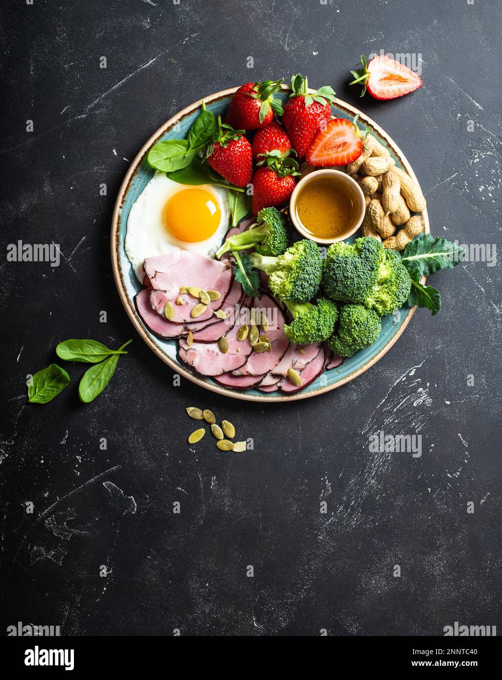 Concept de régime à faible teneur en glucides cétogènes, vue du dessus. Assiette sur fond noir de pierre avec des aliments de céto: Oeuf, viande, huile d'olive, brocoli, baies, noix, graines Banque D'Images