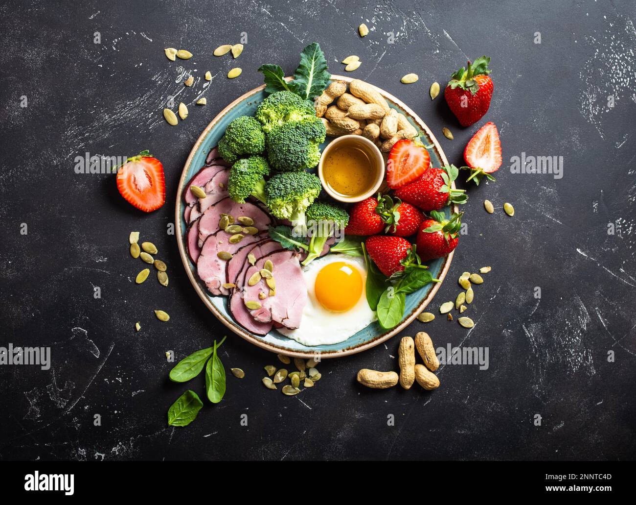 Concept de régime à faible teneur en glucides cétogènes, vue du dessus. Assiette sur fond noir de pierre avec des aliments de céto: Oeuf, viande, huile d'olive, brocoli, baies, noix, graines Banque D'Images