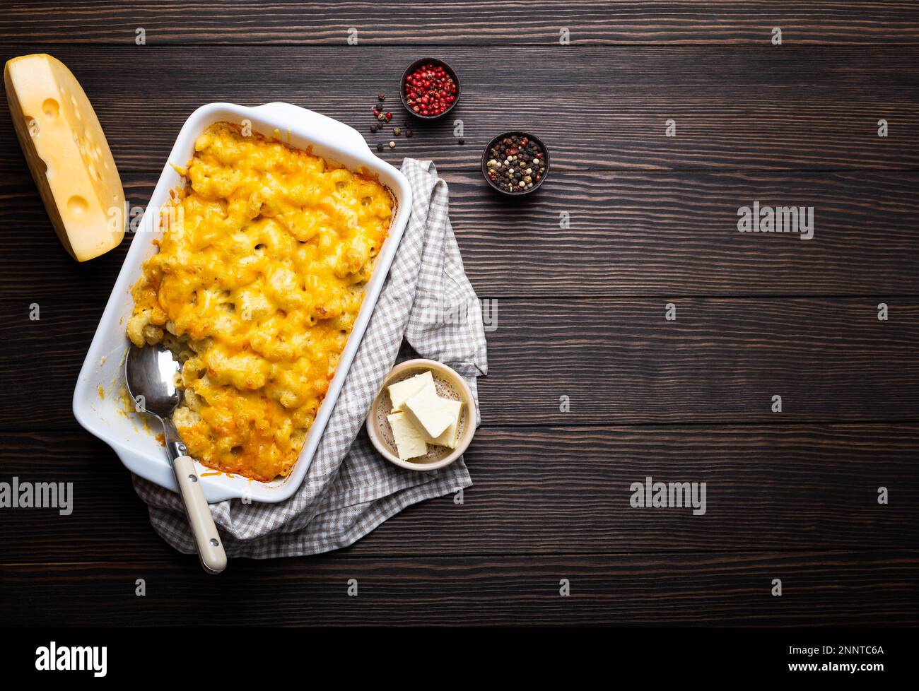 Gros plan de macaroni cuit au four et de fromage dans une casserole blanche sur fond de bois, avec assaisonnements, beurre, cuillère et fourchette, vue de dessus, espace pour le texte. Banque D'Images