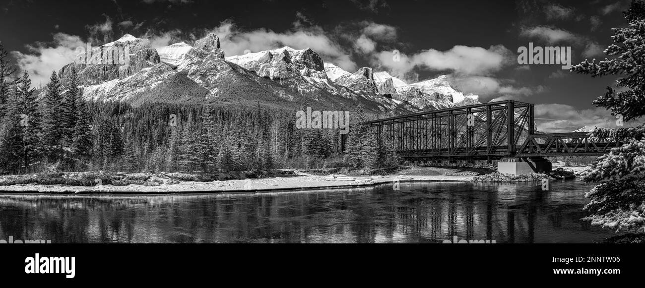 Pont ferroviaire au-dessus de la rivière Bow dans un paysage de montagne enneigé en noir et blanc, Alberta, Canada Banque D'Images