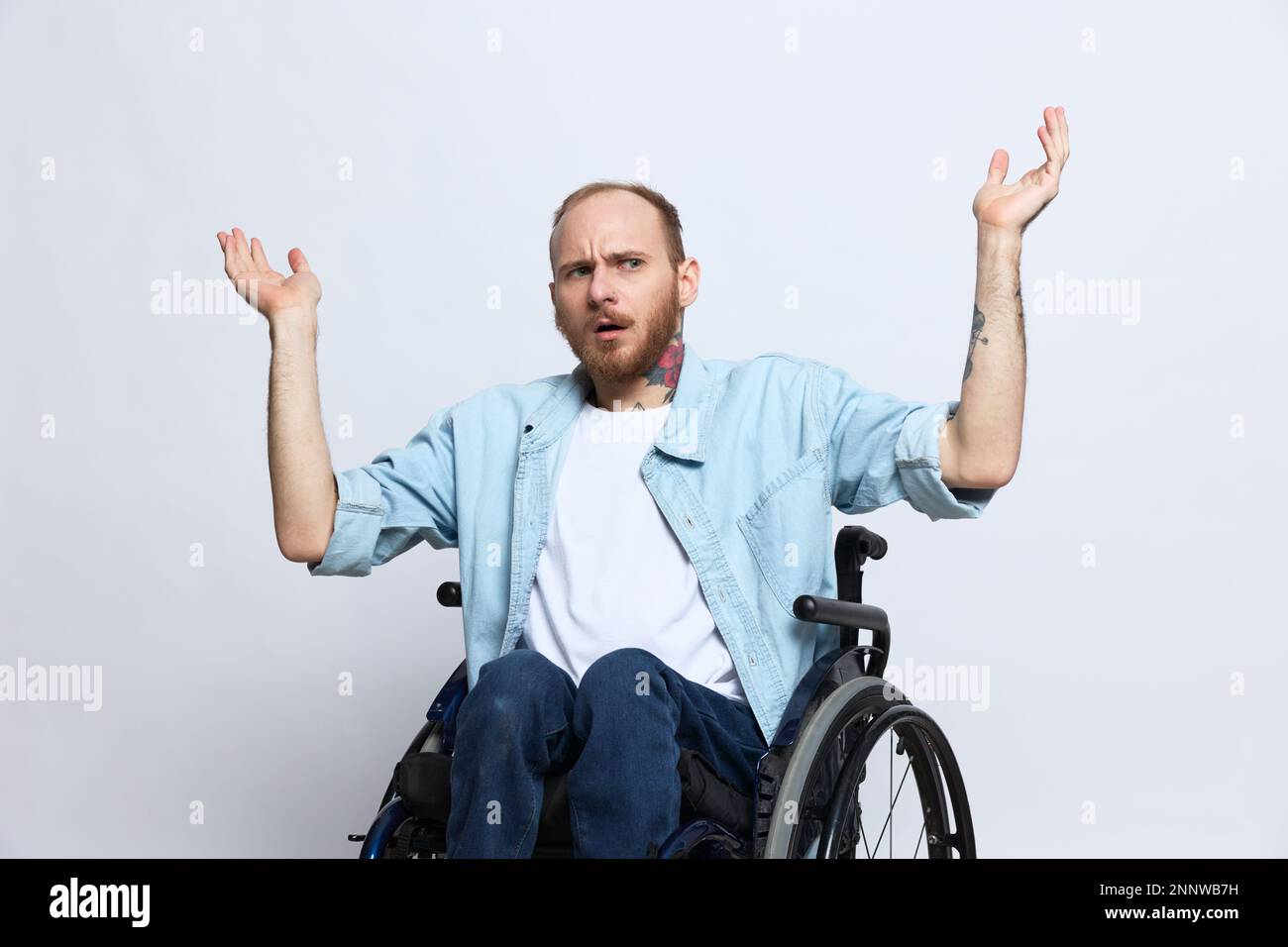 Un homme dans un fauteuil roulant et pointant un doigt, un espace de copie, avec des tatouages sur ses mains est assis sur un fond gris studio, concept de santé une personne avec Banque D'Images