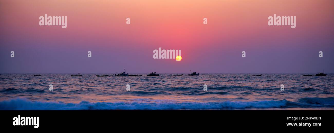 Mer sous ciel moody au coucher du soleil avec des bateaux éloignés, Colva Beach, Margao, Goa, Inde Banque D'Images