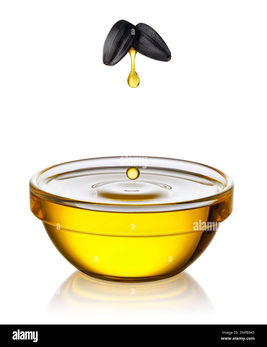 goutte d'huile de tournesol tombant des graines volantes dans un bol en verre isolé sur blanc Banque D'Images