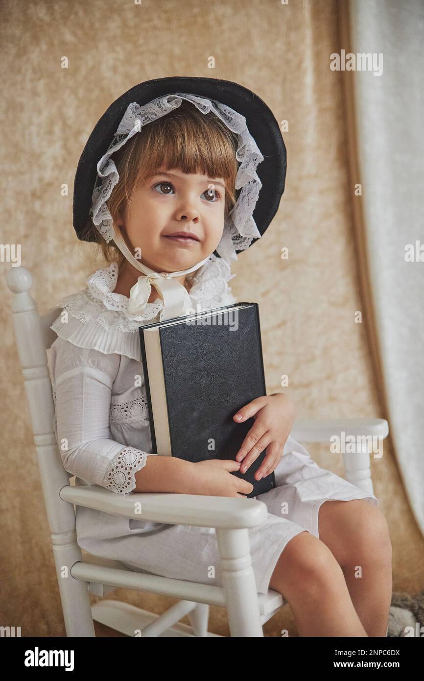 Portrait rétro d'un bel enfant dans un fauteuil à bascule avec livre Banque D'Images