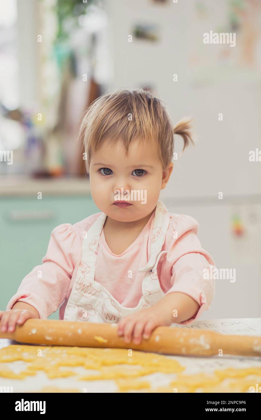 Un adorable bébé dans un tablier roule la pâte dans la cuisine Banque D'Images