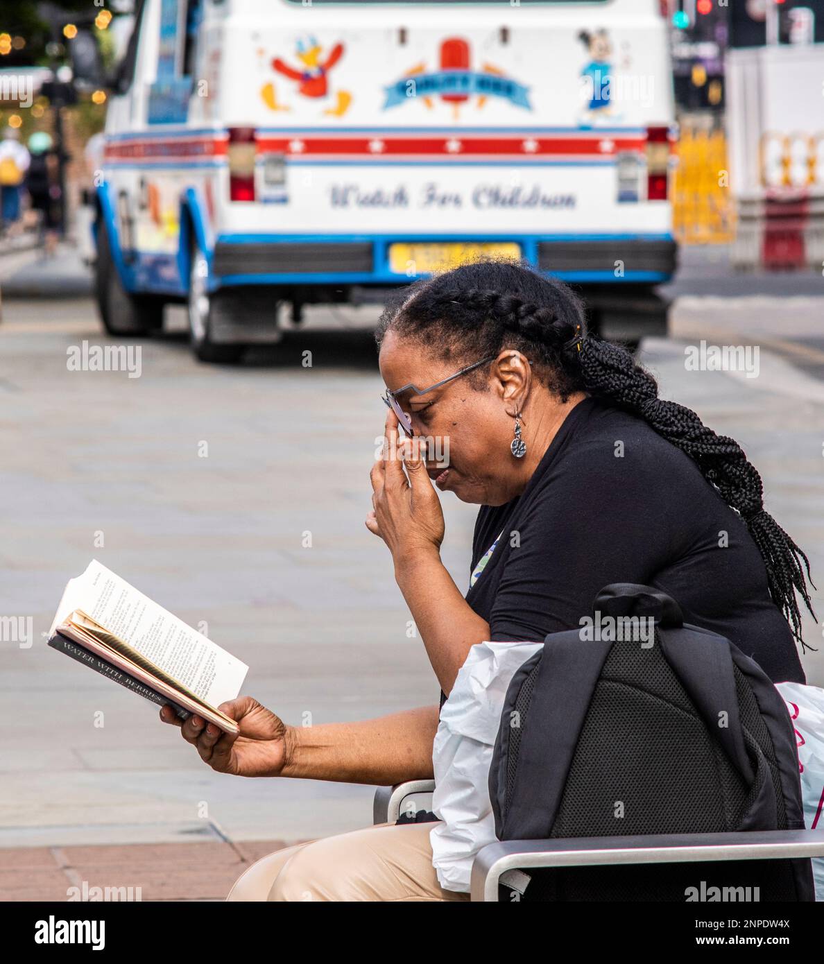 Une dame lit un livre sur un banc à Kings Cross à Londres. Banque D'Images