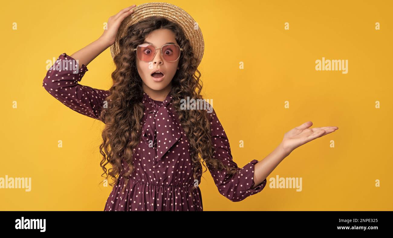 enfant émerveillé dans un chapeau de paille et des lunettes de soleil avec de longs cheveux bruns de présentation du produit Banque D'Images