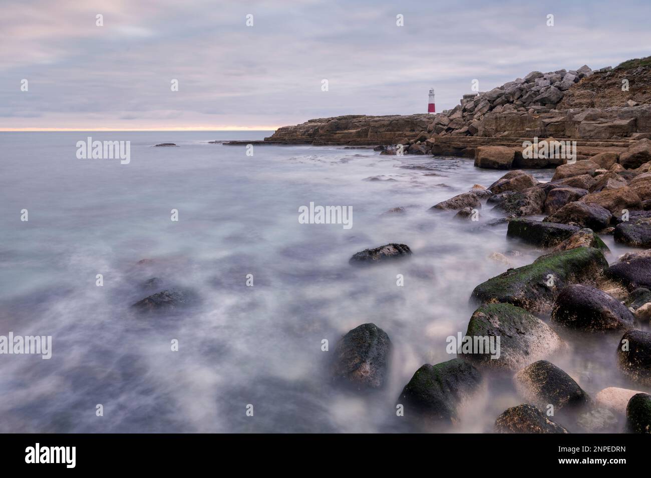 Vagues se lavant au-dessus de rochers de premier plan avec un phare en arrière-plan. Banque D'Images