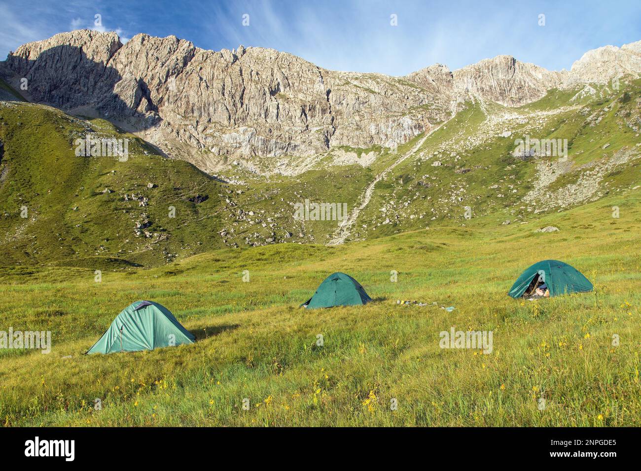 trois tentes sur un pré dans les montagnes sous un mur de roche Banque D'Images