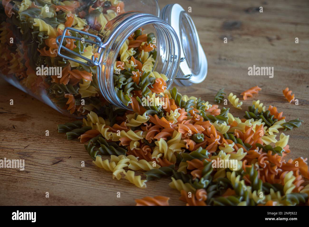 Pot en verre retourné et ouvert sur une table en bois d'où proviennent les spirales de pâte de légumes de couleur Banque D'Images