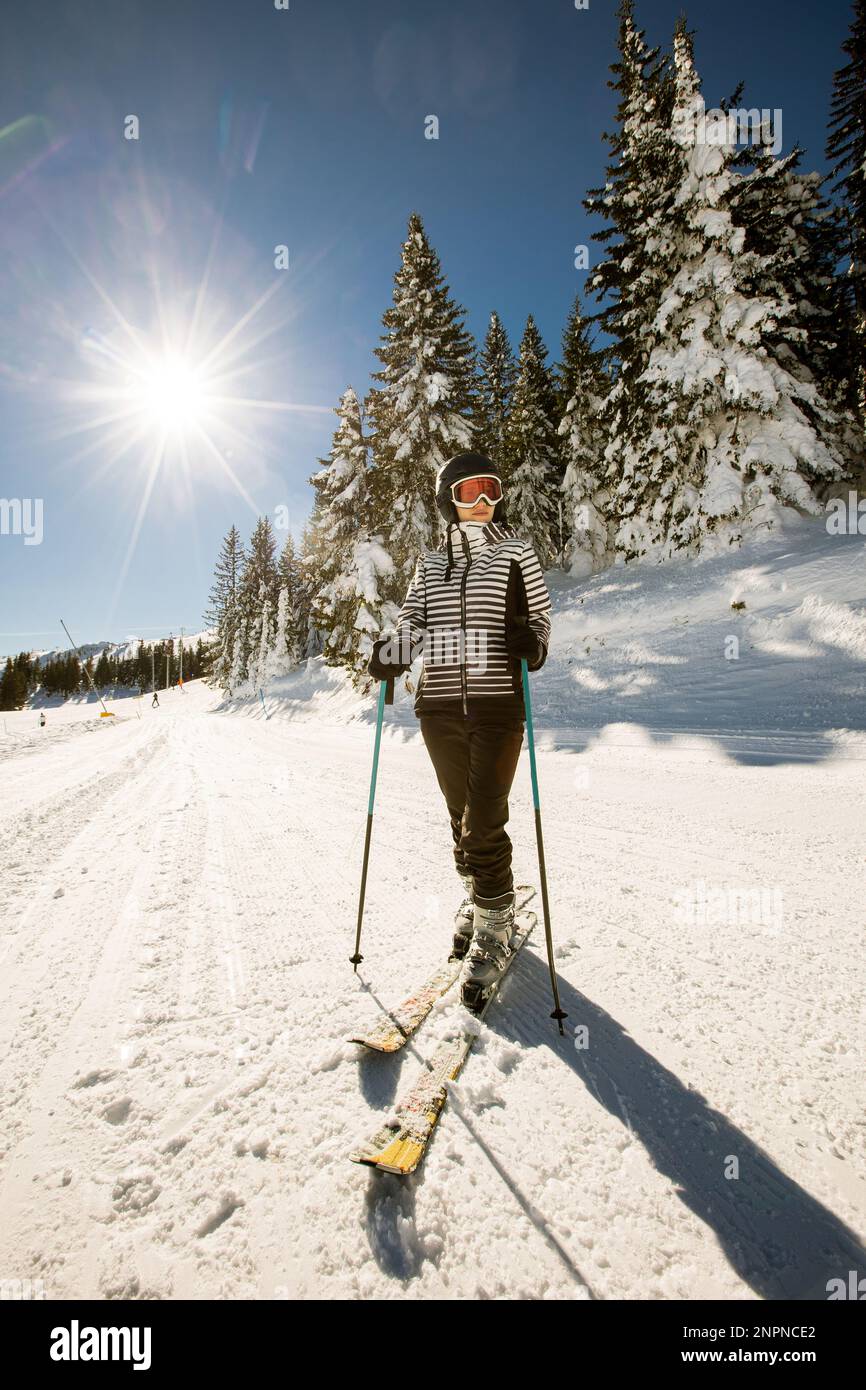 Jeune femme qui profite de la journée d'hiver pour skier sur les pistes enneigées, entourée de grands arbres et habillée pour les températures froides Banque D'Images