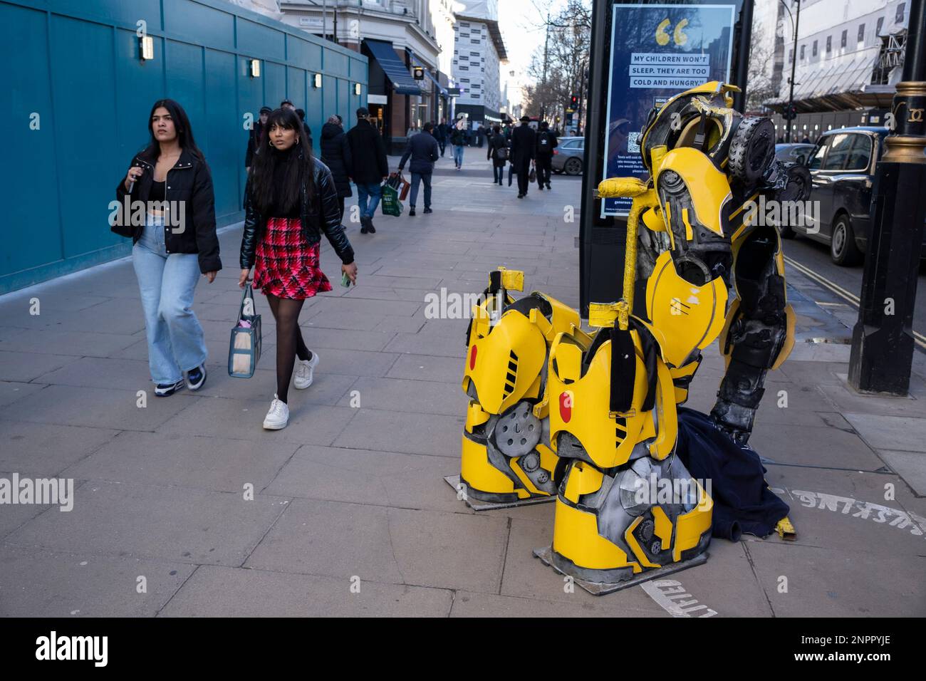 Les passants d'Oxford Street interagissent avec le costume vide d'un interprète de rue qui se présente comme un transformateur jaune le 6th février 2023 à Londres, au Royaume-Uni. Transformers est une franchise de médias produite par la société américaine de jouets Hasbro et la société japonaise de jouets Takara Tomy. Il suit principalement les Autobots héroïques et les dédecepticons vilains. Banque D'Images