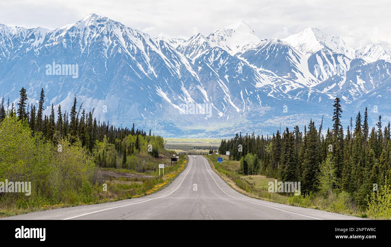 Route de l'Alaska en voiture dans la ville de Haines Junction au printemps avec des montagnes énormes et épiques à distance avec une incroyable route panoramique en avant. Banque D'Images