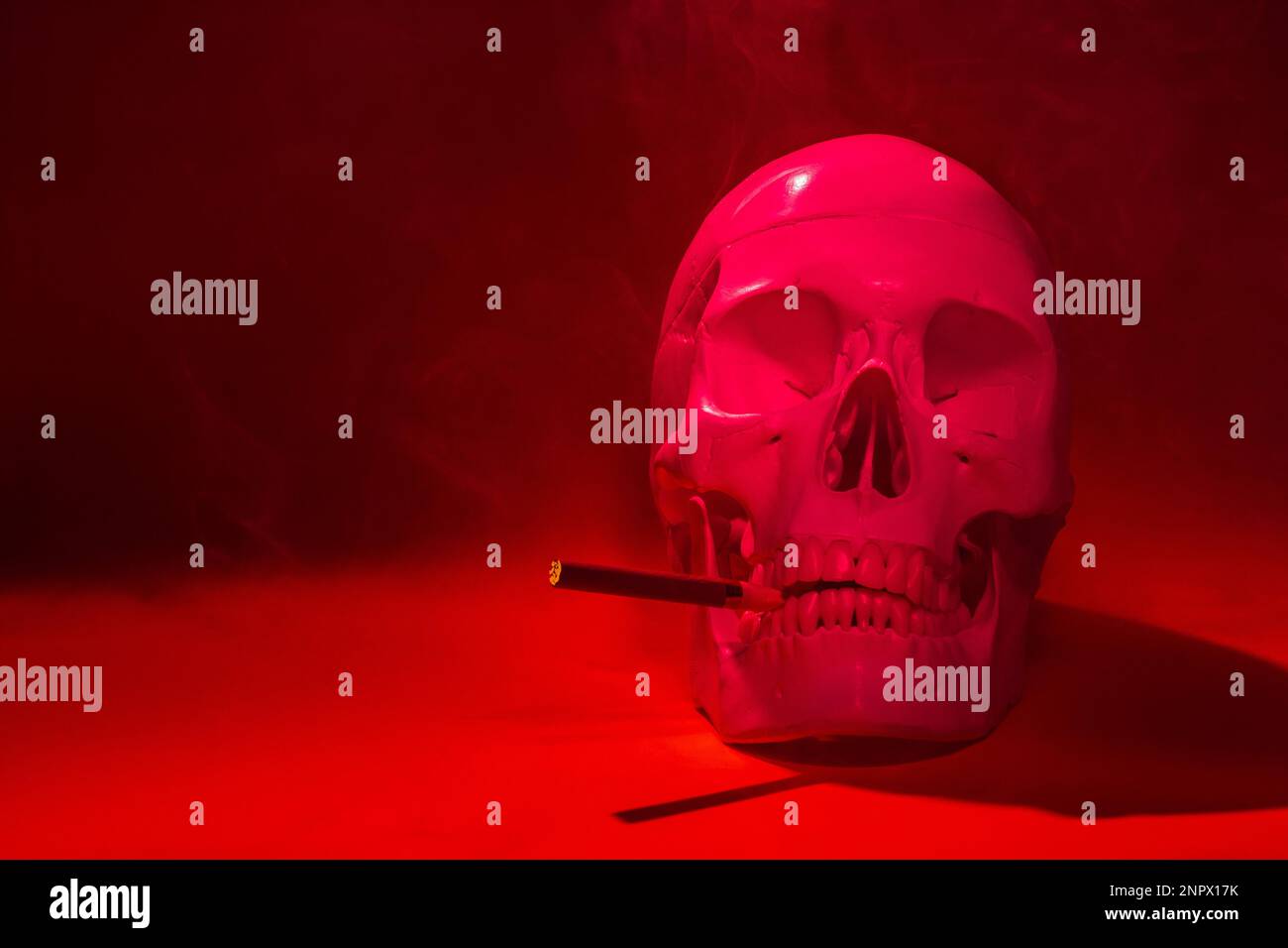 crâne d'un homme avec un squelette d'os de cigarette, un objet, sinistre horreur terrible, rouge en couleur, avec une cigarette brûlante dans la fumée. concept mort f Banque D'Images