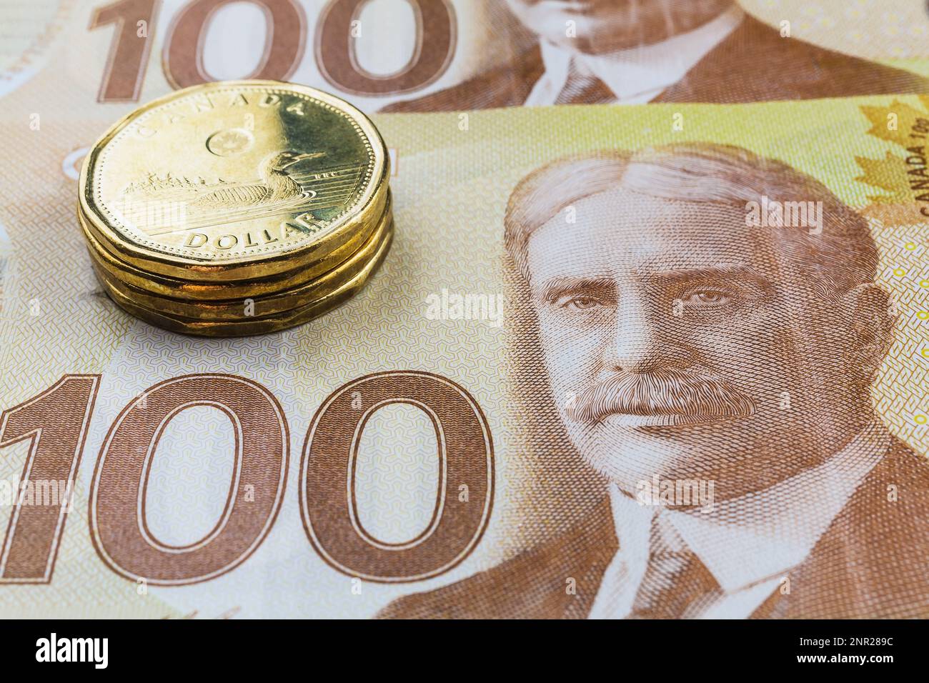 Pile de pièces de un dollar canadien sur les billets de banque de cent dollars canadiens. Banque D'Images