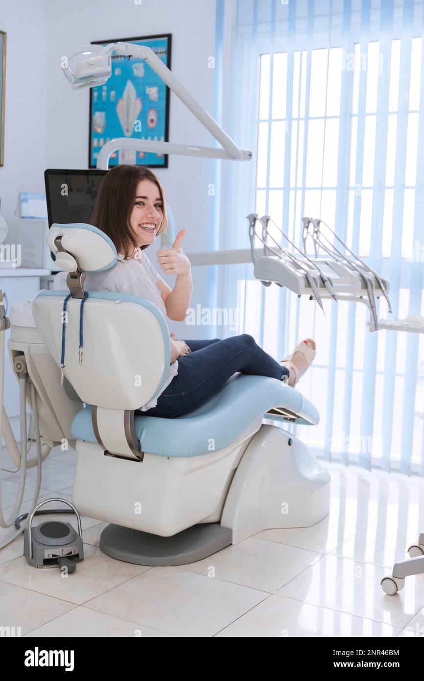 femme souriante assise chaise montrant le pouce vers le haut clinique dentaire. Photo haute résolution Banque D'Images