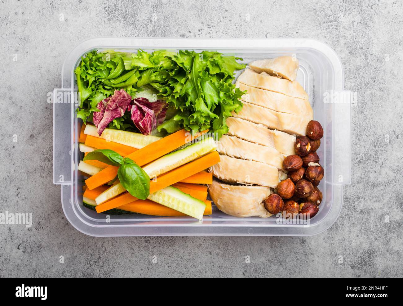 Une boîte à lunch pour le bureau ou l'école avec des aliments sains : filet de poulet, bâtonnets de carottes et de concombres, salade, noix. Préparation et emballage des repas préparés en Banque D'Images