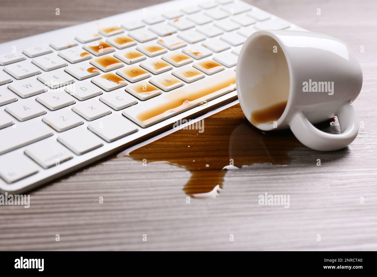 Tasse de café renversée sur le clavier de l'ordinateur sur une table en bois Banque D'Images Tasse de café renversée sur le clavier de l'ordinateur sur une table en bois Banque D'Images