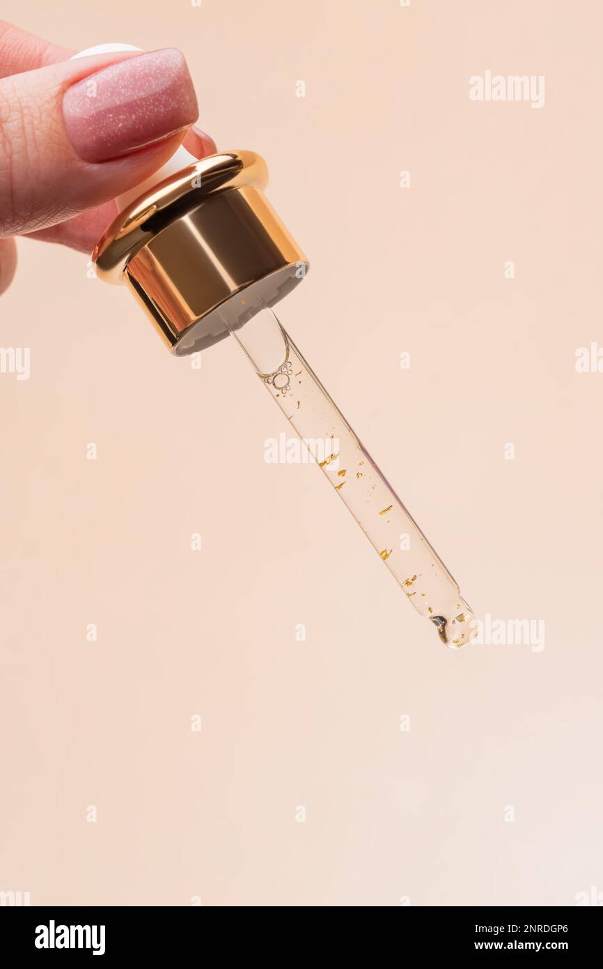 Main femelle avec Dropper d'huile essentielle, essence d'aromathérapie, sérum de beauté avec 24K d'or ou liquide médicinal sur fond beige. Flacons sans marque Banque D'Images