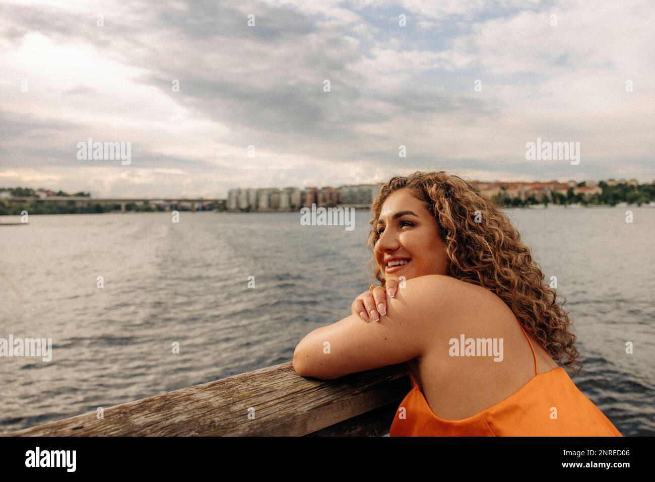 Une femme heureuse avec des cheveux bouclés penchés sur la main contre le ciel Banque D'Images