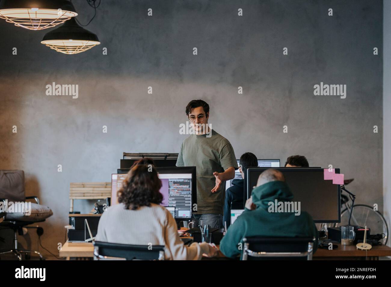 Jeune hacker masculin discutant avec des collègues masculins et féminins travaillant sur l'ordinateur dans la société de démarrage Banque D'Images