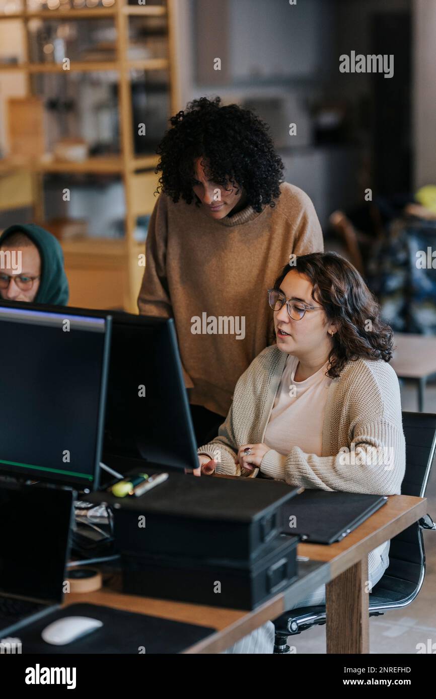 Collègues professionnels multiraciaux discutant sur ordinateur au bureau Banque D'Images