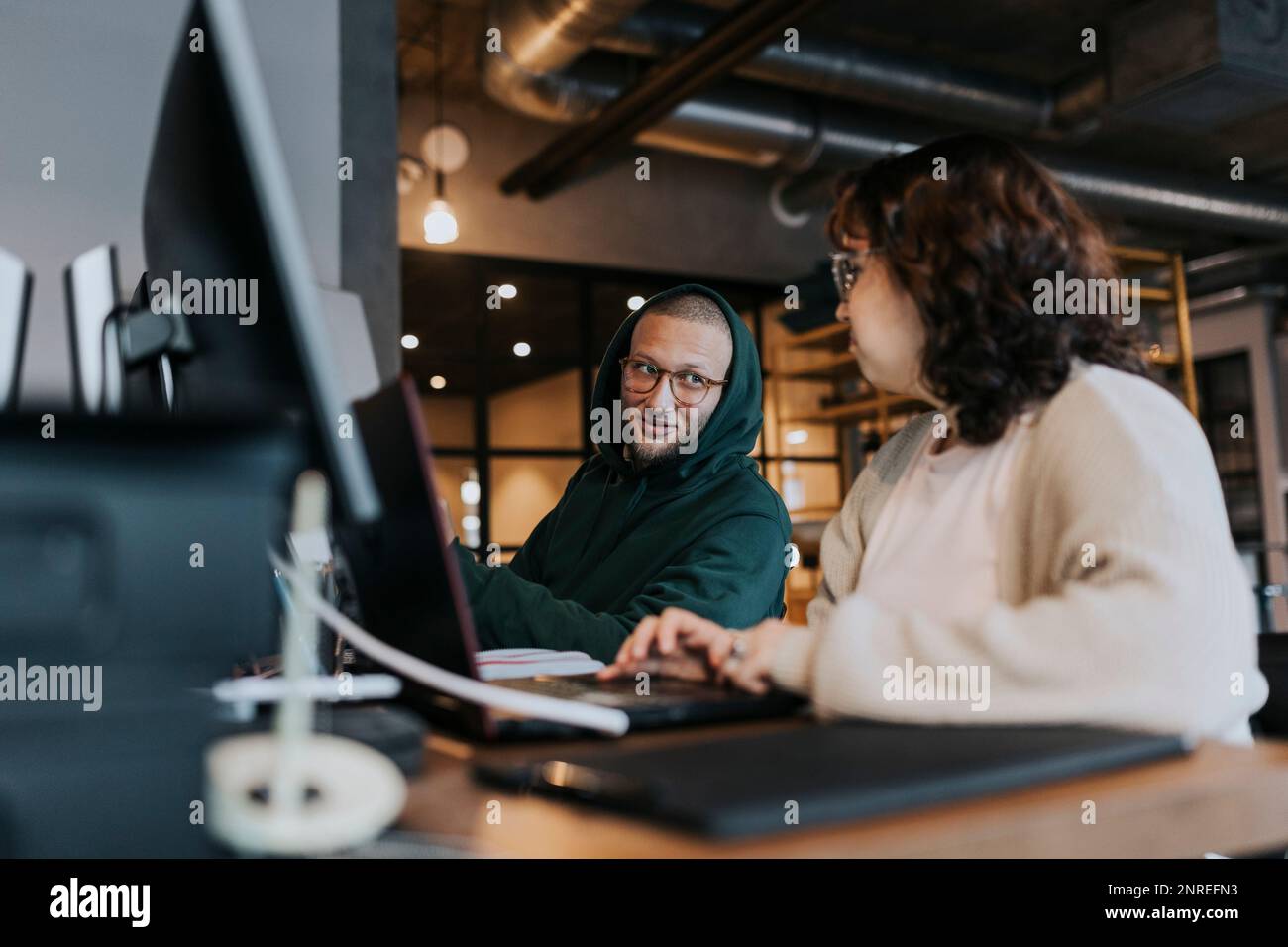 Un jeune hacker masculin discute avec une collègue féminine à son bureau dans un lieu de travail créatif Banque D'Images