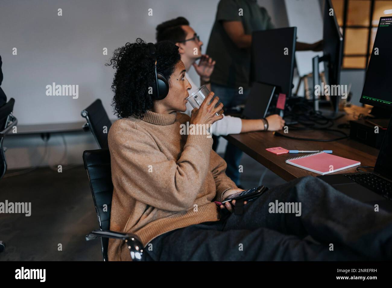 Femme d'affaires buvant du café tout en regardant le hacker d'ordinateur travaillant dans la société de démarrage Banque D'Images