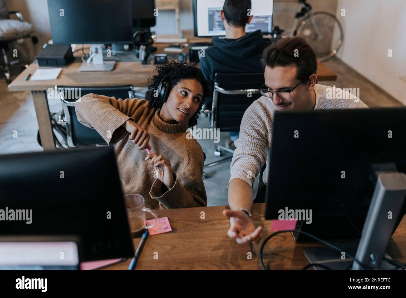 Un hacker masculin souriant discute avec une collègue féminine à la réception dans un bureau de création Banque D'Images