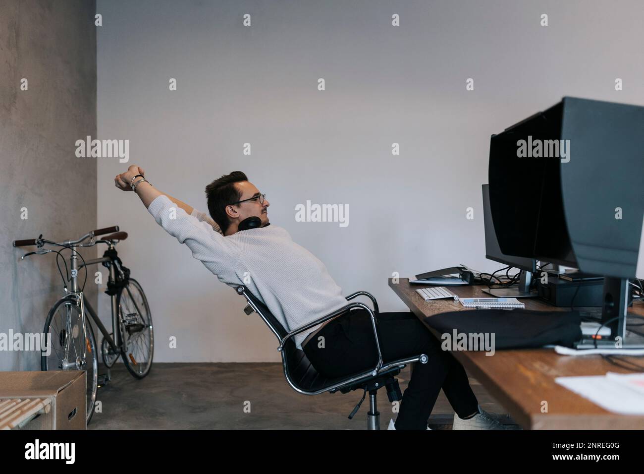 Un jeune hacker mâle étire les mains tout en travaillant sur un ordinateur dans une entreprise de démarrage Banque D'Images