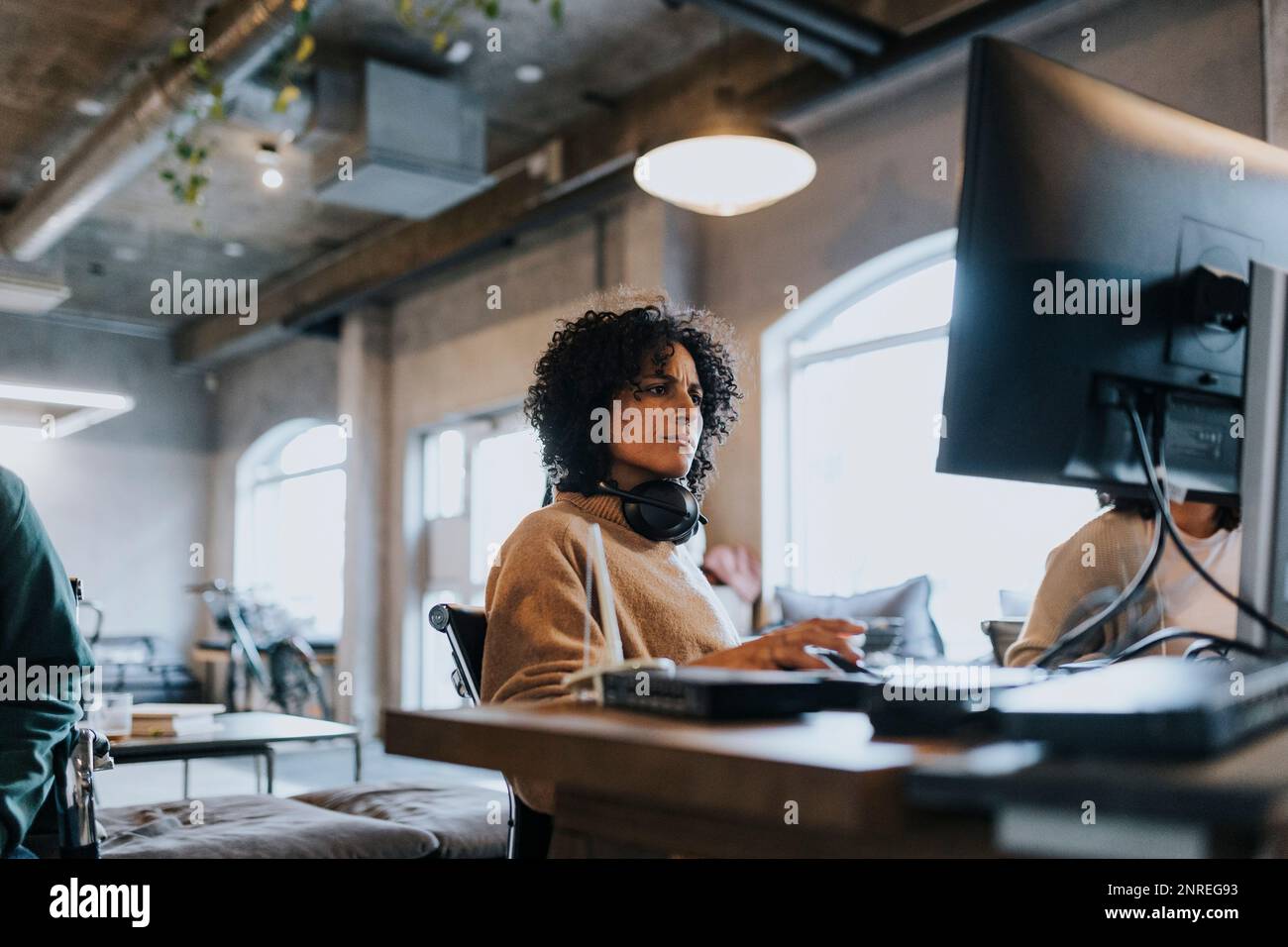 Hacker féminin avec casque sans fil autour du cou en utilisant un ordinateur pendant le travail au bureau Banque D'Images