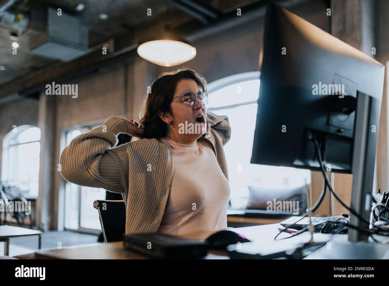 Une femme fatiguée qui hurle et s'étire les mains au bureau dans un bureau créatif Banque D'Images