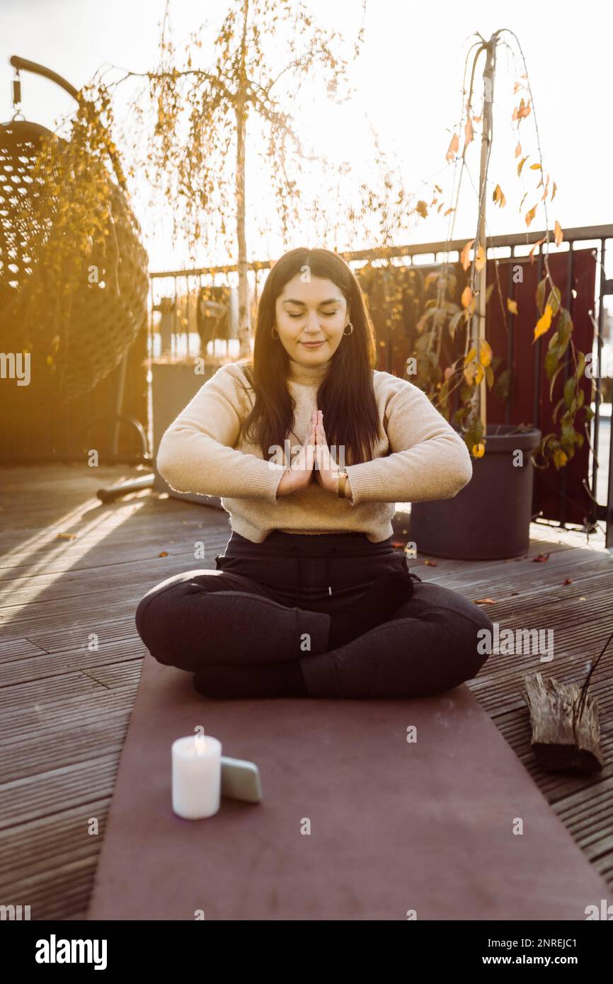 Femme faisant du yoga en étant assise avec les mains clastées sur le tapis d'exercice sur la terrasse Banque D'Images