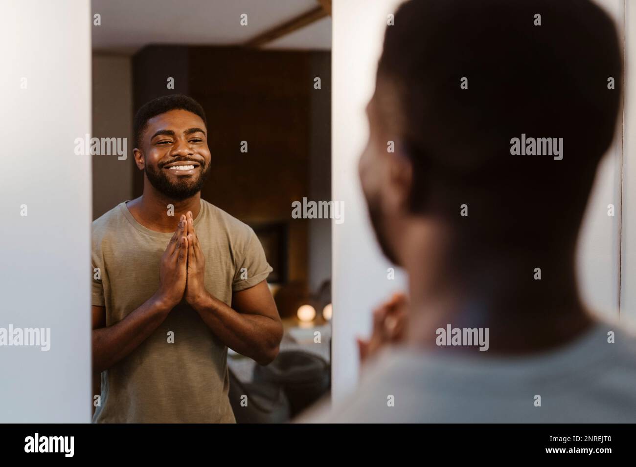 Homme souriant avec les mains jointes regardant dans le miroir à la maison Banque D'Images