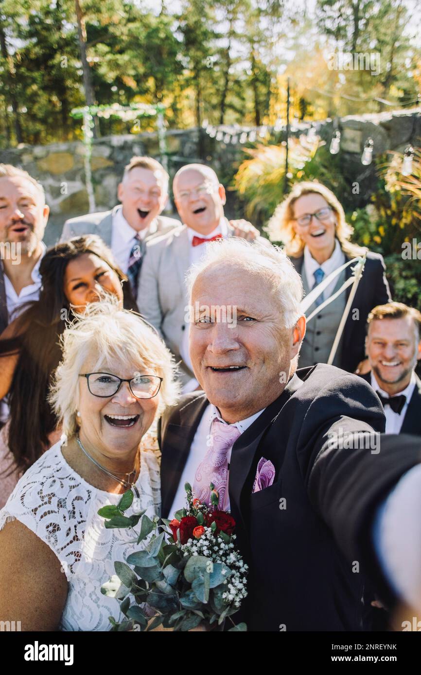 Couple senior jeune et joyeux prenant le selfie avec la famille et les amis lors du mariage Banque D'Images