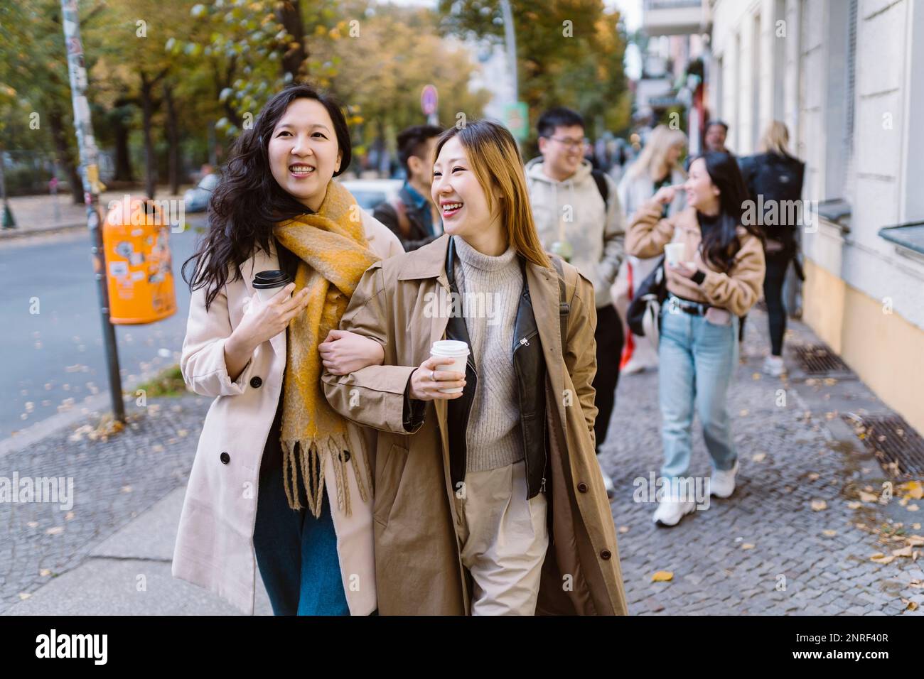 Des amies souriantes marchant avec le bras dans le bras tout en marchant sur le trottoir Banque D'Images