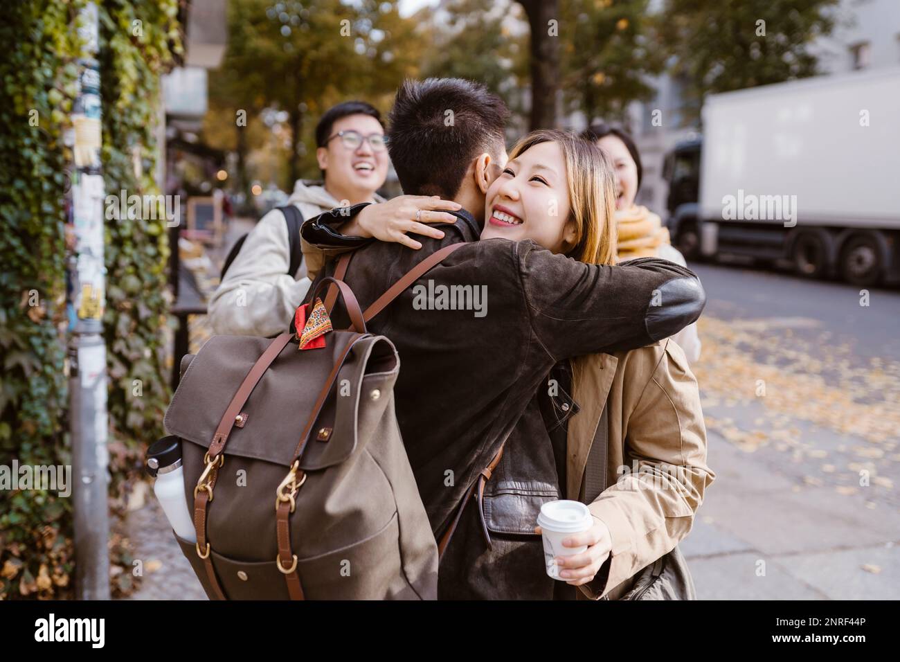 Une jeune femme heureuse embrassant un ami masculin portant un sac à dos tout en se tenant sur le trottoir Banque D'Images Une jeune femme heureuse embrassant un ami masculin portant un sac à dos tout en se tenant sur le trottoir Banque D'Images