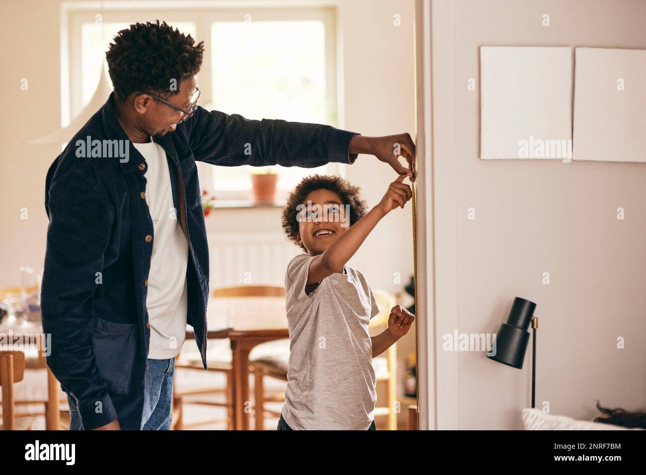 Fils souriants regardant le père tout en vérifiant la hauteur à la maison Banque D'Images