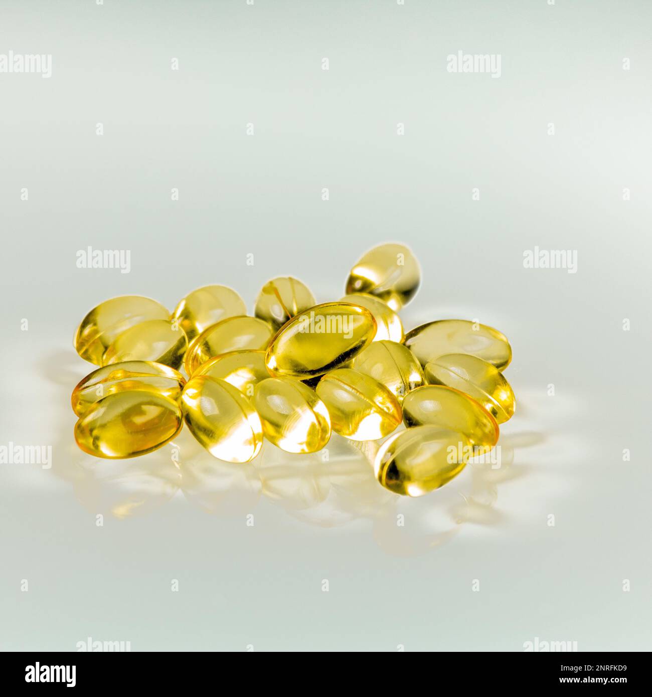 Pile de capsules de gel d'huile de poisson jaune réfléchie sur fond de verre. Banque D'Images