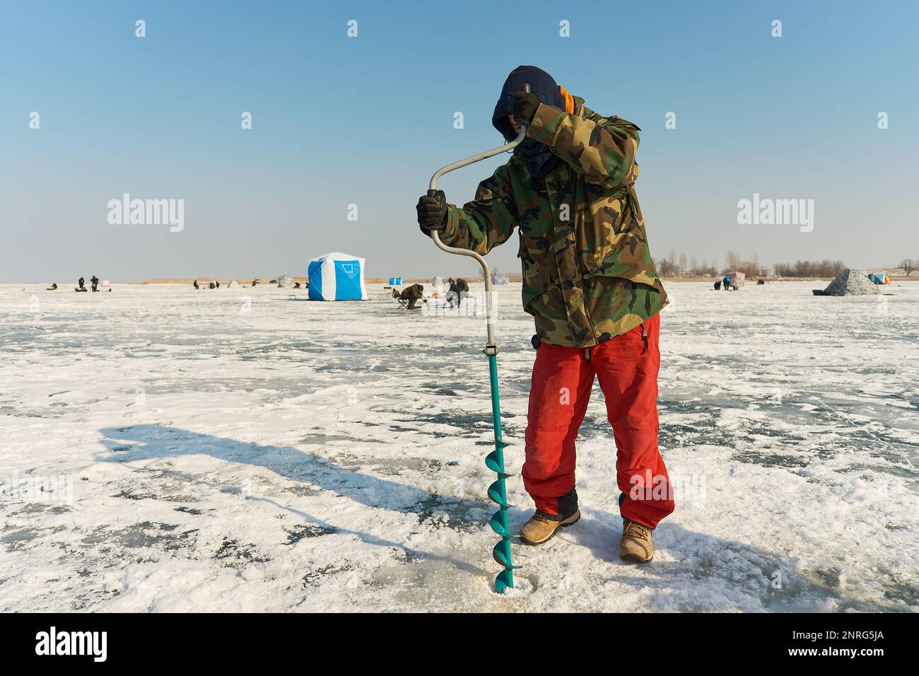 Un homme asiatique aux couleurs chaudes fore un trou dans la glace en hiver Banque D'Images