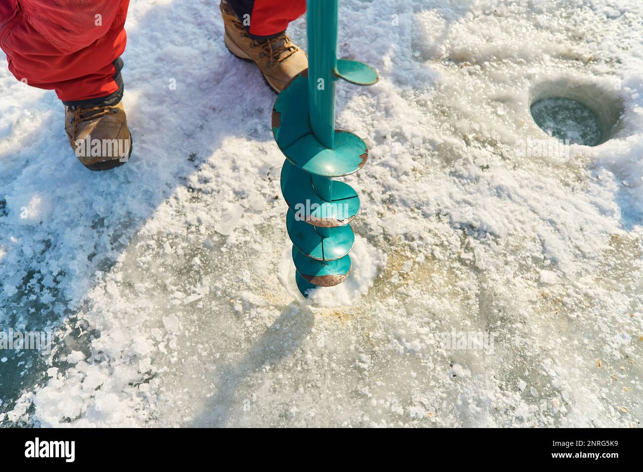 Un homme asiatique aux couleurs chaudes fore un trou dans la glace en hiver Banque D'Images