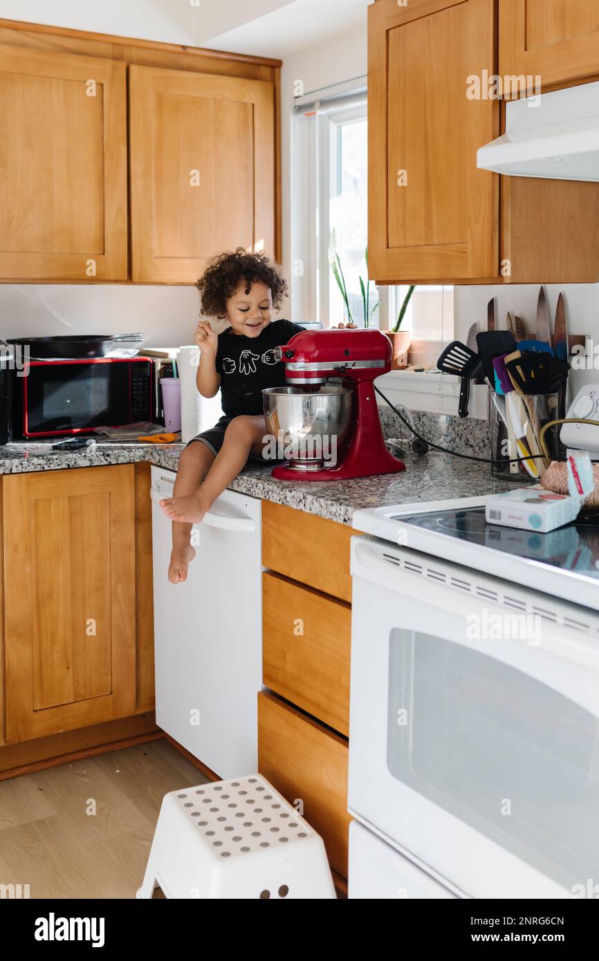 Petit garçon biracial assis sur un comptoir de cuisine avec biscuits Banque D'Images