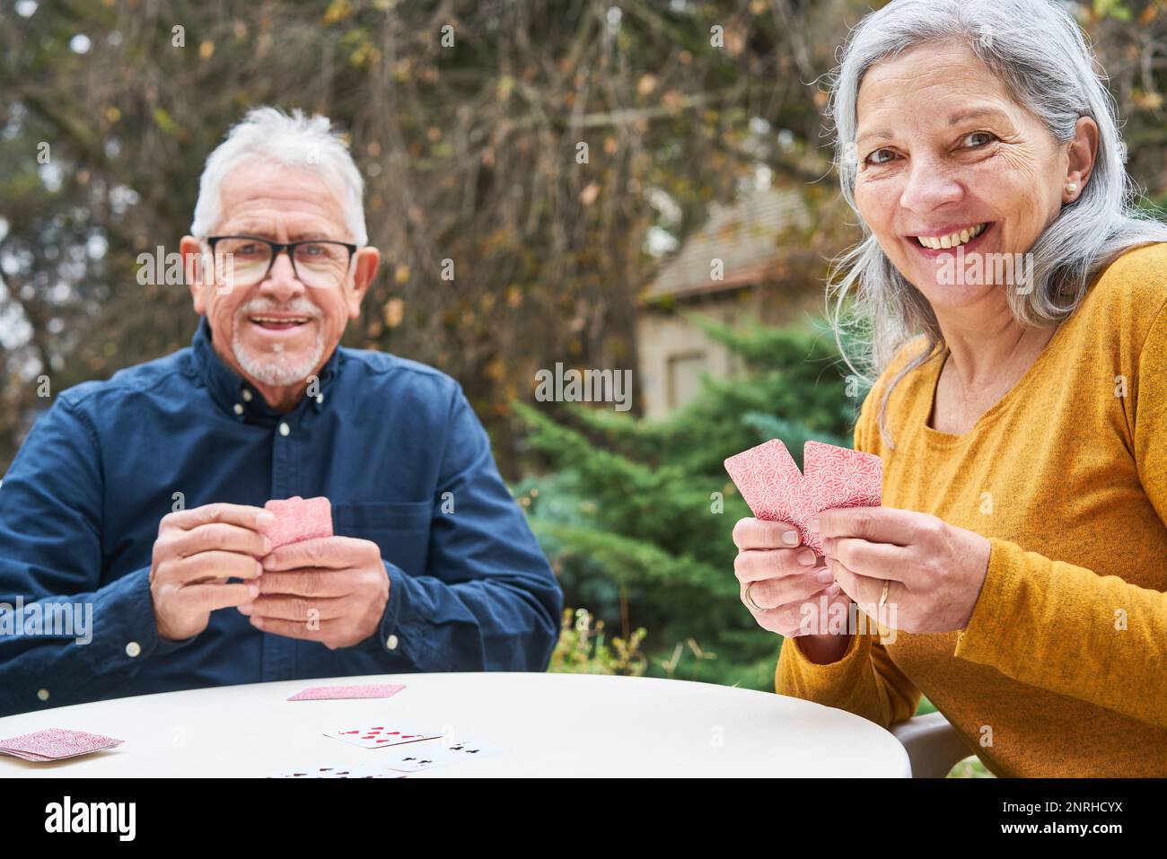 Portrait d'un homme et d'une femme âgés jouant aux cartes tout en étant assis à une table dans le jardin de la maison de retraite Banque D'Images