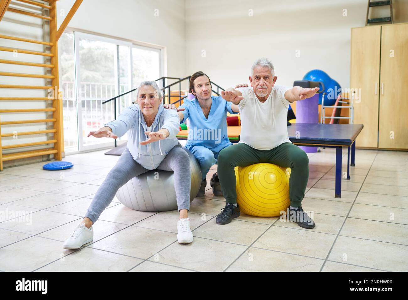 Physiothérapeute masculin avec des personnes âgées s'exerçant sur le ballon de fitness dans la salle de gym Banque D'Images