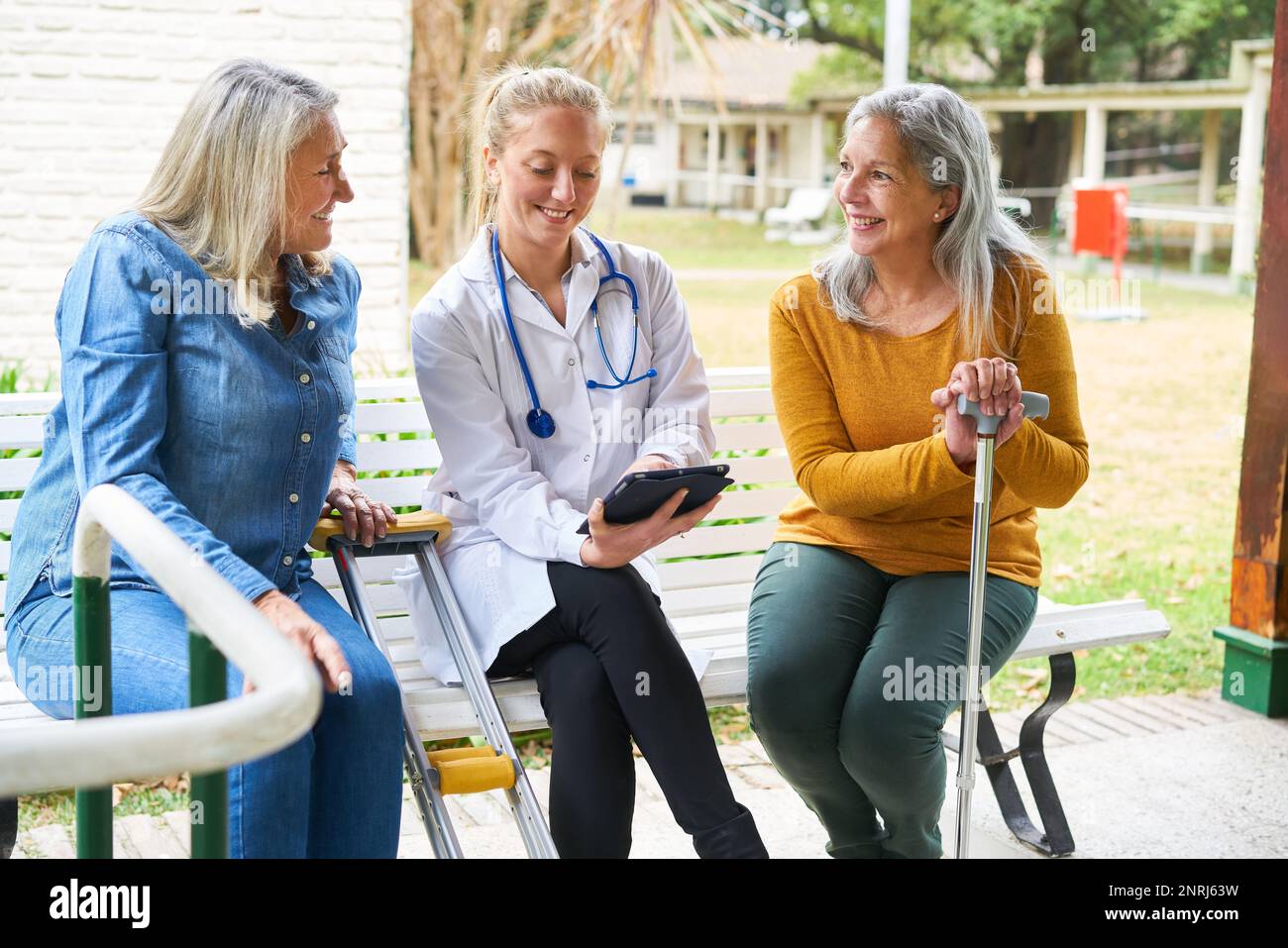Une infirmière souriante explique les femmes âgées au-dessus d'un PC tablette dans le jardin de la maison de retraite Banque D'Images