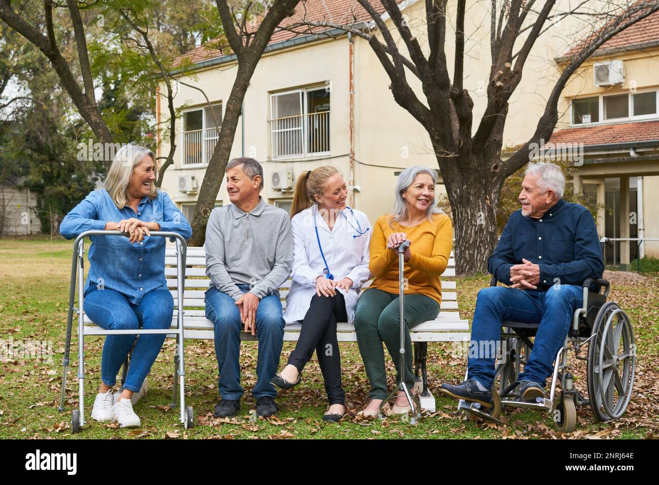 Joyeux médecin parlant à un groupe de personnes âgées assis sur un banc dans le jardin de la maison de soins infirmiers Banque D'Images