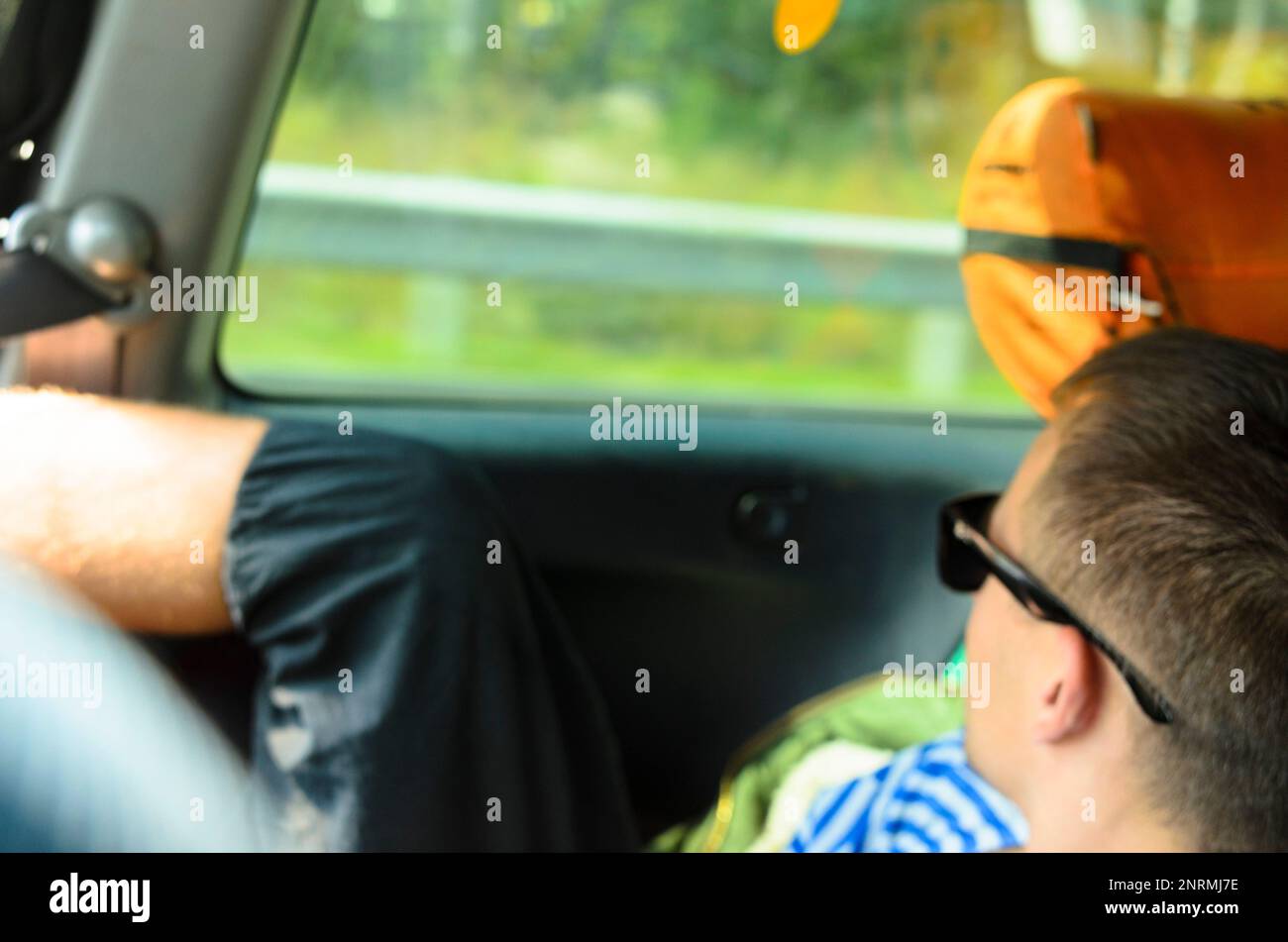 Flou de mise au point photo d'un homme au repos dans des lunettes sombres regardant à travers la fenêtre d'une voiture dans le siège arrière parmi les choses touristiques. Banque D'Images