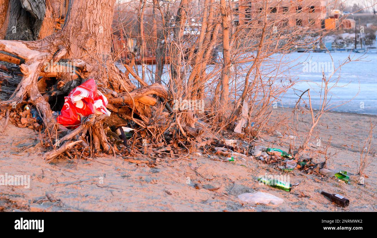 Une montagne de déchets avec un paquet de bouteilles en verre et en plastique se trouve sur la rive d'une rivière de la ville au printemps en Russie. Banque D'Images