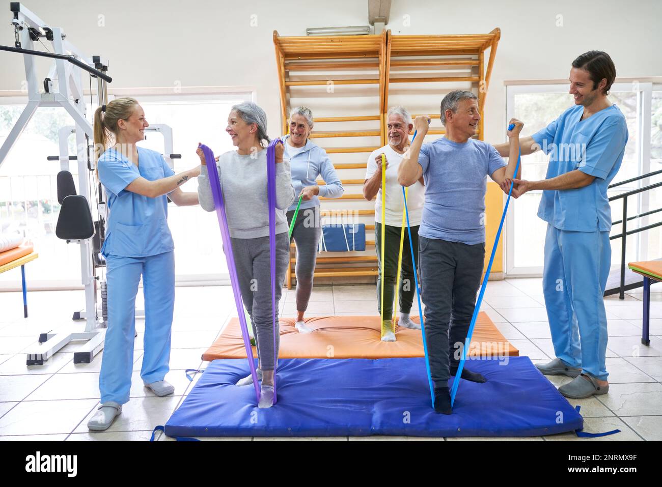 Des physiothérapeutes souriants aident les personnes âgées à faire de l'exercice avec des bandes élastiques au centre de réadaptation Banque D'Images